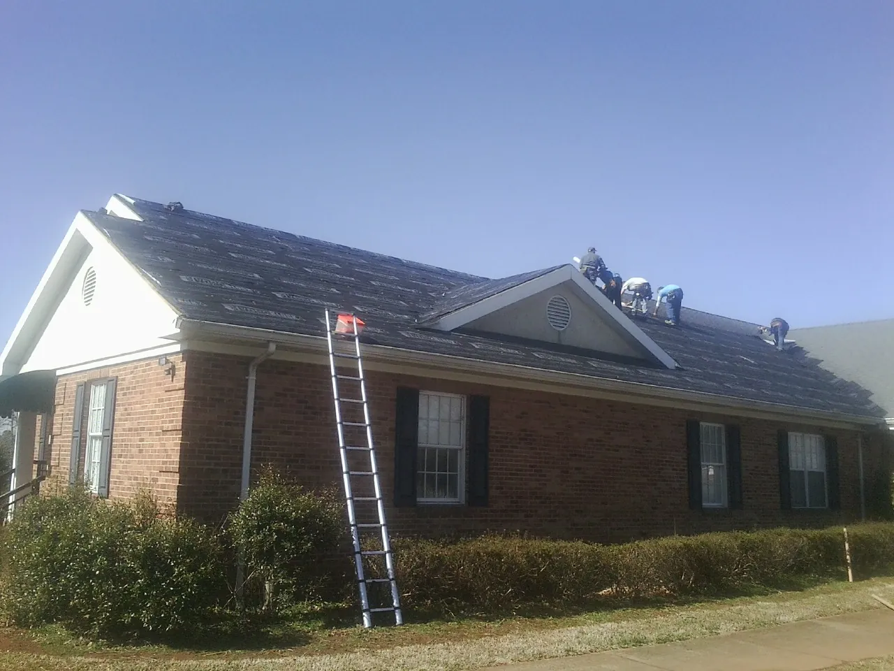 Crew tearing shingles off a brick ranch roof with a ladder set — Emergency Roof Repair work by our crew in Star Junction