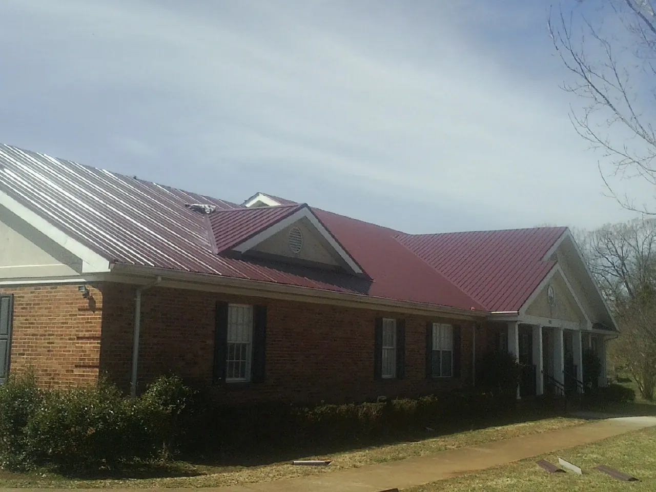 Red metal roof with gabled entries on a long brick building, from a Hail Damage Roof Repair job in Star Junction