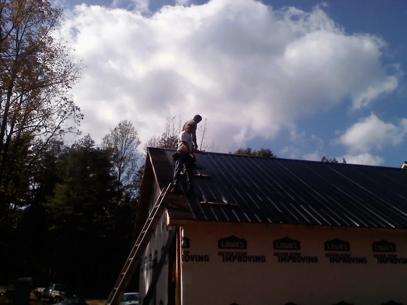 Roofer fastening dark metal panels high against a cloudy sky, from a Roof Inspection job in Star Junction