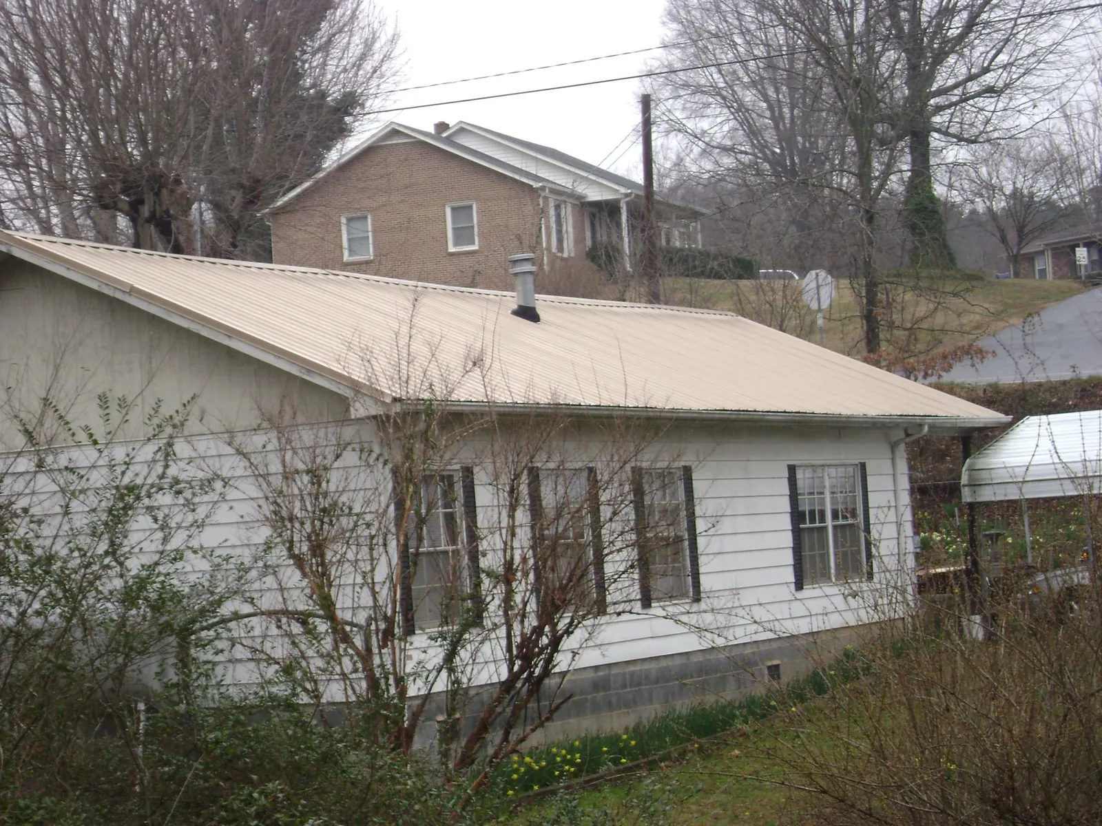 Tan metal roof on a white sided house set into a hillside — Commercial Roofing by Roofing Brothers in Star Junction